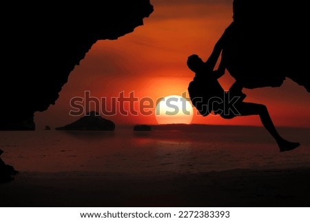 Asian man climbing a cliff by the sea As the sun sets around the islands in the Gulf of Thailand, Koh Samui