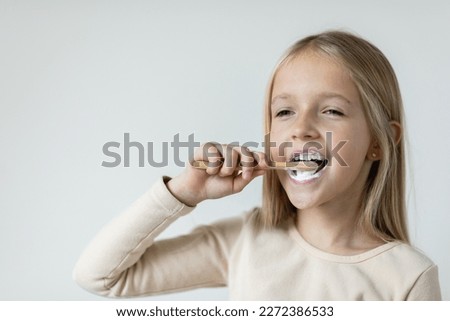 Cute little girl holding hands eco bamboo toothbrush on beige background. Sustainable living concept. Save the Planet for our children