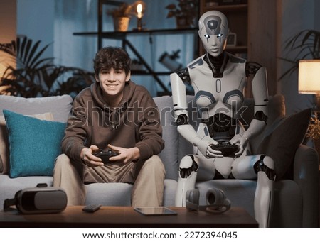 Happy teenager and AI robot sitting on the couch at home, they are playing video games together