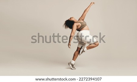 Young woman dancing in a studio, wearing fitness clothing. Young female expressing her self-assurance and body confidence, effortlessly finding her flow in a body movement. Royalty-Free Stock Photo #2272394107