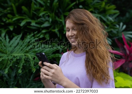 girl in the park or in nature uses a mobile phone, looks at the screen, smile and communication 