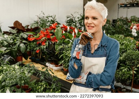 Woman taking care of potted plants. Woman florist thinking. Smiling middle aged female model with house plant. Agriculture and gardener concept. Attractive successful nursery owner in her greenhous.