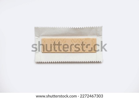 A piece of chewing gum in an unpacked wrapper on a white background. Flavored chewing gum is used after meals to freshen breath and clean teeth. The habit of chewing gum. Royalty-Free Stock Photo #2272467303