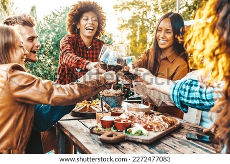 Multiracial friends having fun at barbecue dinner party in garden restaurant - Millennial people cheering red wine sitting at outside bar table - Youth lifestyle, food and beverage concept