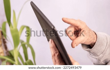 Internet communication. Elderly mature woman is using tablet computer, chatting, talking on video call, reading e-book, watching movie, listening to music, media content while sitting at home.
