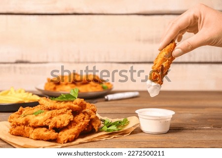 Woman dipping tasty nugget into sauce on wooden table Royalty-Free Stock Photo #2272500211