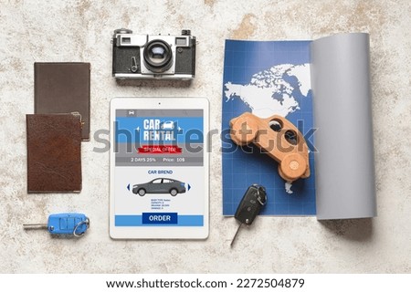 Tablet computer with open page of car rental website, map, keys, photo camera and passports on light background