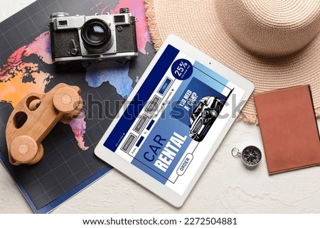 Tablet computer with open page of car rental website, map, photo camera, hat and passport on white background