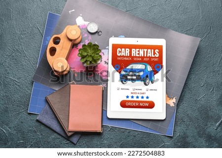 Tablet computer with open page of car rental website, maps and passports on dark background