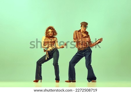 Feeling rhythm. Couple happy people, man and woman in retro style clothes dancing disco dance over green background. Concept of 1970s, 1980s fashion, music, hippie lifestyle Royalty-Free Stock Photo #2272508719