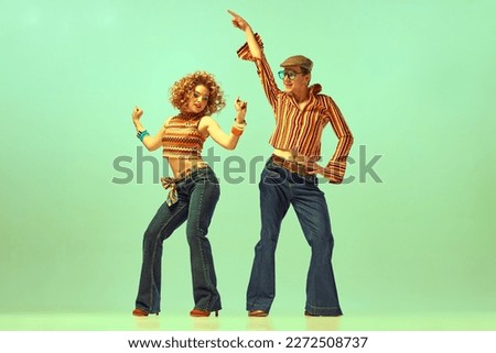 Happy and active dancers. Two excited people, man and woman in retro style clothes dancing disco dance over green background. 1970s, 1980s fashion, music, hippie lifestyle Royalty-Free Stock Photo #2272508737