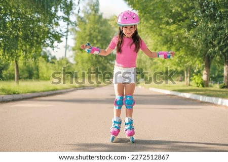 A beautiful preschool girl in a protective sports helmet and roller skates rides on an asphalt path on a hot summer morning.  The child learns new skills and learns sports