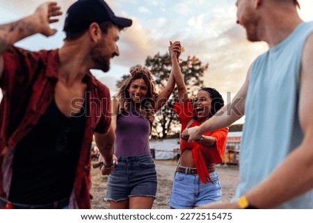A group of young cheerful friends are bonding at a summer festival in a beautiful sunset, dancing and singing together.