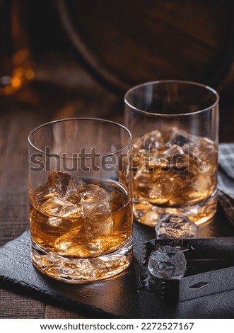 Two glasses of whiskey with ice on a black slate board with wooden background Royalty-Free Stock Photo #2272527167