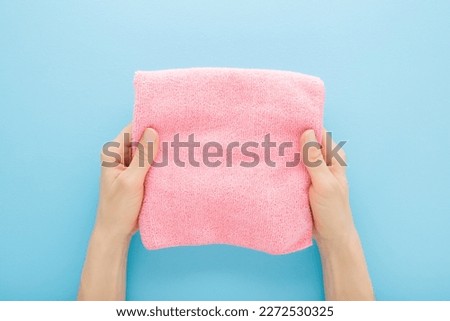 Young adult woman hands holding pink folded dry soft microfiber rag for different surfaces wiping. Closeup. Light blue table background. Pastel color. Point of view shot. Royalty-Free Stock Photo #2272530325
