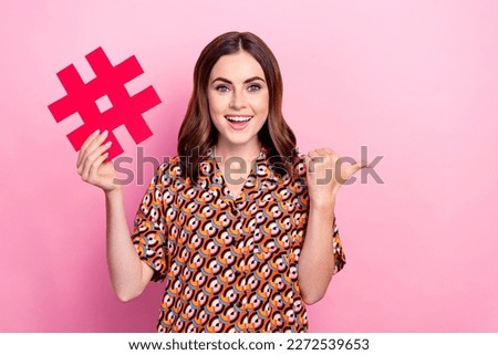 Photo of youngster funny optimistic girl wear shirt excited hold paper hashtag point finger empty space subscribe isolated on pink color background