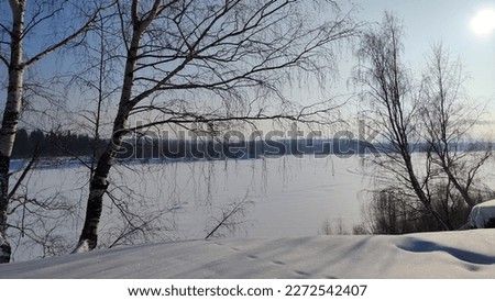 Winter landscape with trees on a cliff and view from height of frozen river or field with snow on cold sunny day with blue sky Royalty-Free Stock Photo #2272542407