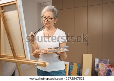 Slender elderly lady paints a picture in a spacious room