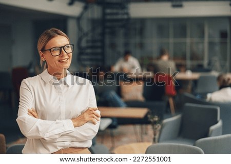 Portrait of successful woman manager standing with crossing hands in office on colleagues background