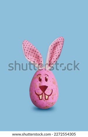 Easter bunny egg decoration with bunny ears and bunny face on pastel blue background. Perfect for Easter greeting cards, social media posts, and web banners