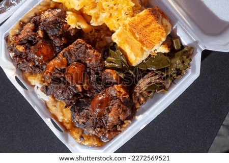 A top down view of an entree of smothered oxtails, with a side of mac n cheese, corn bread, and collard greens. Royalty-Free Stock Photo #2272569521