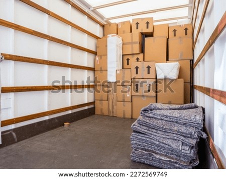 The inside of a removal van, showing fabric blankets stacked and a background of cardboard boxes. Concept for moving home, furniture protection, storage, packing and transportation. Copy space. Royalty-Free Stock Photo #2272569749