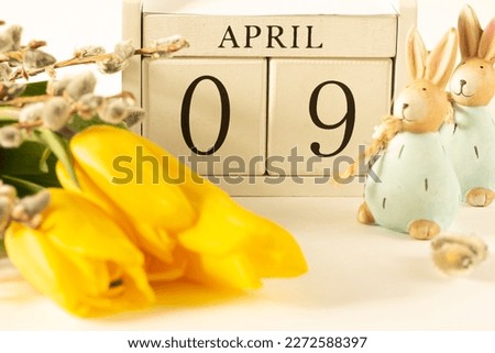 April Easter. White block calendar presents month April,  date 9th, Easter rabbits and spring flowers on white background.