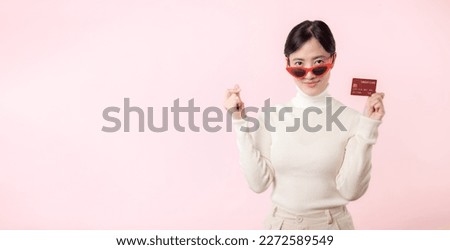 Fascinating joyful fun young woman of Asian ethnicity 20s years old with wear sunglasses wears white shirt hold in hand credit bank card isolated on plain pastel light pink background studio portrait. Royalty-Free Stock Photo #2272589549