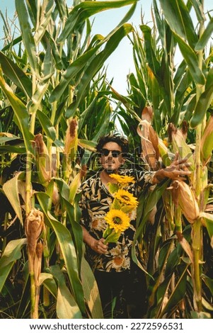 Rock and roll embraces nature: young rocker enjoys sunny day in a corn field with bouquet of sunflowers