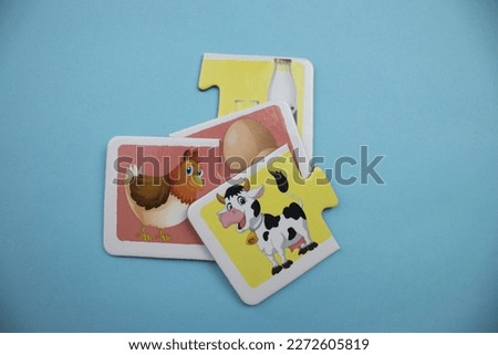 Cow picture puzzle in black and white, knowledge puzzles with pictures of brown chicken, white egg, black and white cow and milk bottle placed on a blue background.