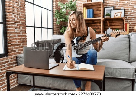 Young blonde woman smiling confident playing electric guitar at home