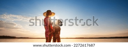 Mother and child are looking at seascape at sunset. Family summer vacation at sea concept. Warm rays of sunlight. Back view.