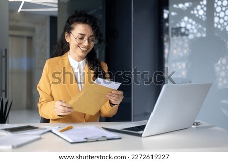 Successful hispanic woman inside office at work businesswoman received postal envelope letter notification with good news, female worker celebrating victory and good results achievement at workplace. Royalty-Free Stock Photo #2272619227