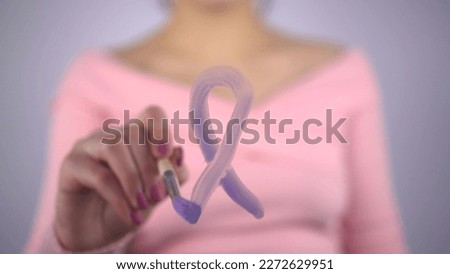 A woman draws a loop of lavender color on the glass, meaning all types of cancer. The girl draws with a brush on a transparent glass.