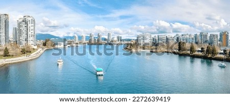 Touristic waterfront city panorama on a sunny spring day with modern highrise buildings, boats, water taxi, sunday walkers and mountain background. False Creek, Vancouver, BC, Canada. Selective focus. Royalty-Free Stock Photo #2272639419