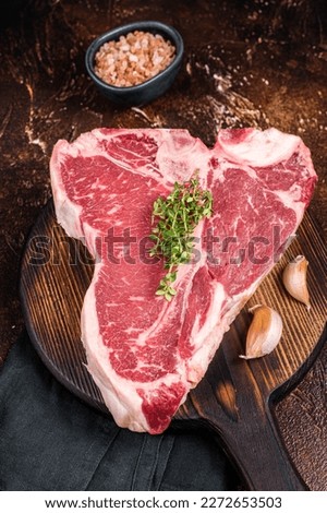 Raw Porterhouse steak, marbled beef meat on a wooden board. Dark background. Top view. Royalty-Free Stock Photo #2272653503