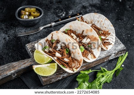 Pork carnitas tacos on corn tortillas with onion and lime. Black background. Top view.