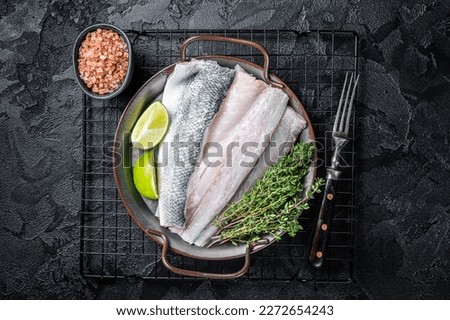 Raw Sea Bass fillet, Labrax fish with herbs and lime. Black background. Top view. Royalty-Free Stock Photo #2272654243