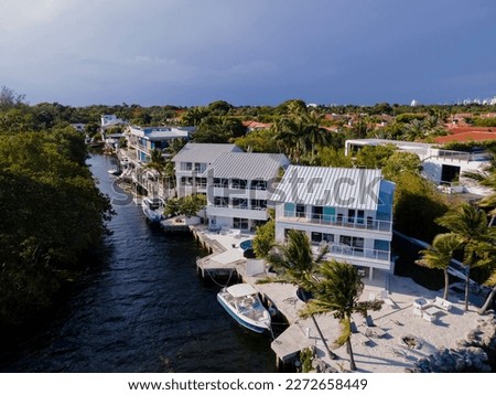 Row of three-storey houses with private docks on the waterway in an aerial view at Miami, Florida. Waterfront homes beside the water near the forest with trees on the right. Royalty-Free Stock Photo #2272658449