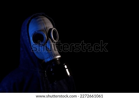 Man in a hood in an old retro gas mask in neon light on a black background