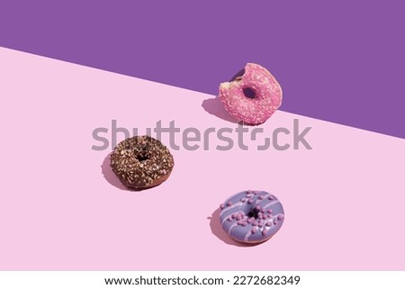 Various colorful glazed doughnuts with sprinkles on a pink background