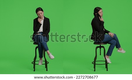 Caucasian businesswoman answering call on smartphone, sitting on chair in studio background. Office worker talking on remote telephone line using mobile phone, full body green screen backdrop.