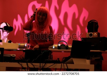 Asian woman with pink hair mixing techno music on turntables while playing record mix sounds in studio with pink background. Performer having fun while performing electronic song, enjoying night life