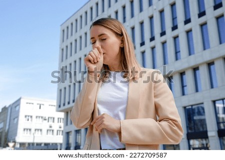 Sick businesswoman in formal wear standing outdoor and coughing. Unwell beautiful caucasian woman having pain in chest. Concept of health problem, virus and infection Royalty-Free Stock Photo #2272709587