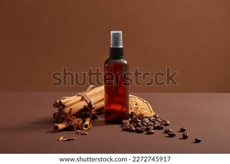 A glass sprayer containing essential oil extracted from coffee beans, star anise, dried orange slices and cinnamon sticks. Promotion of cosmetic product for hair