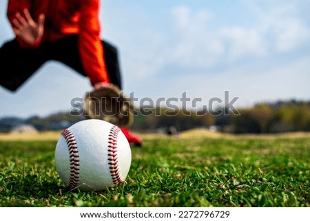 Baseball ball on the lawn. Man in catching position in background. Royalty-Free Stock Photo #2272796729