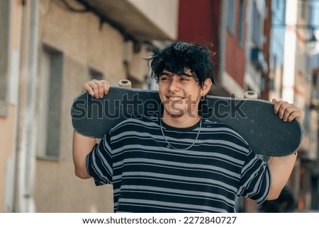 happy teenager walking through the city with skateboard in his hands