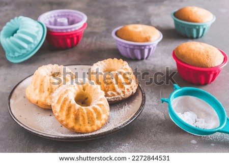 Homemade mini bundt cakes and their colorful silicone cake molds on gray background Royalty-Free Stock Photo #2272844531