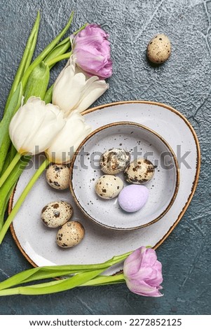 Tulip flowers and bowl with Easter quail eggs on black grunge background