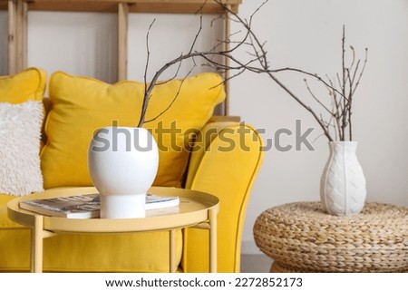 Vase with tree branches and magazine on table in living room, closeup
